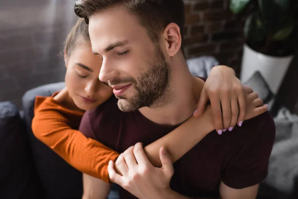 Young man with closed eyes embraced by tender girlfriend on blurred background — Stock Photo