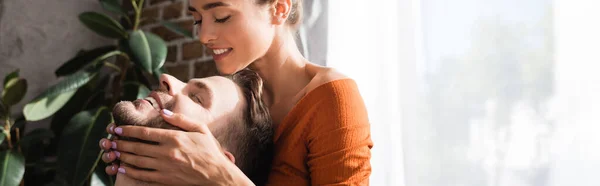 Sonriente mujer tocando la cara de novio feliz con los ojos cerrados, bandera - foto de stock