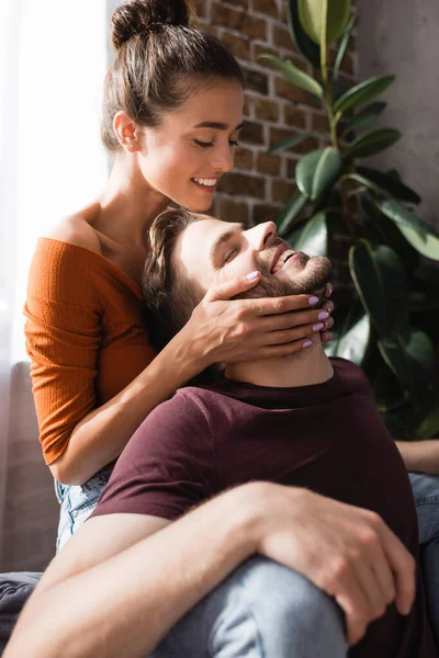 Happy woman touching face of smiling man with closed eyes at home — Stock Photo