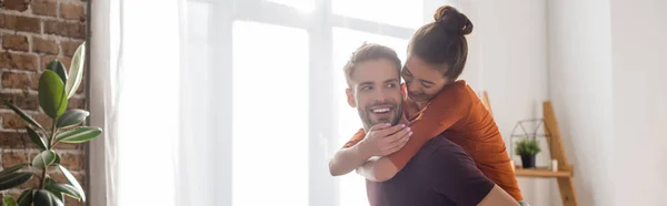 Joyeuse femme piggybacking sur heureux petit ami à la maison, bannière — Photo de stock