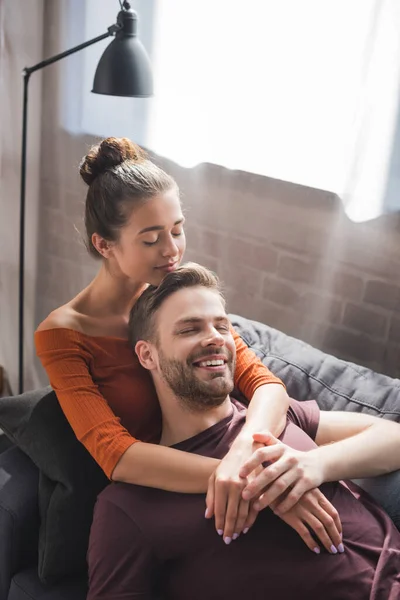 Donna felice che abbraccia il fidanzato sorridente mentre riposa sul divano di casa — Foto stock