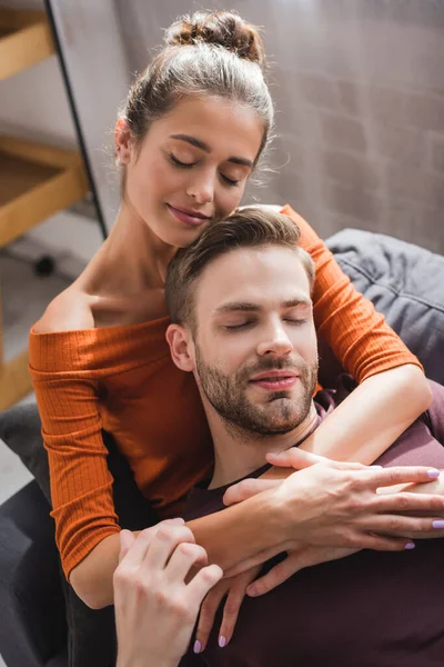 Mujer feliz abrazando novio mientras descansa en el sofá con los ojos cerrados - foto de stock