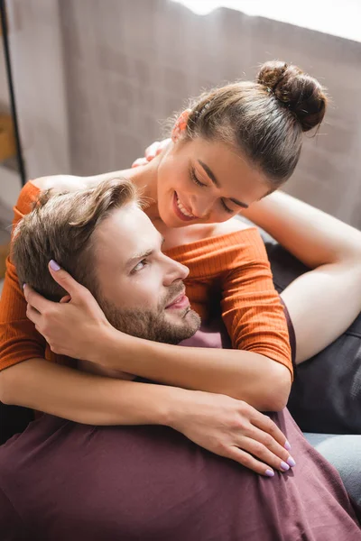 Щаслива, ніжна жінка дивиться на коханого чоловіка, обіймаючи його на дивані вдома — стокове фото