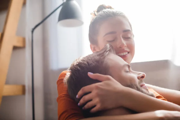 Mujer feliz con los ojos cerrados abrazando la cabeza del hombre amado en casa - foto de stock