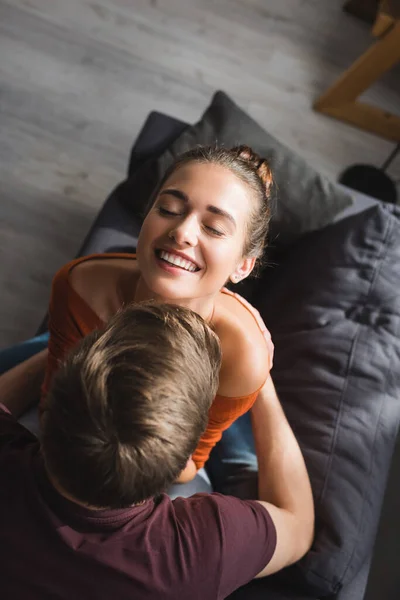 Overhead view of cheerful woman with closed eyes embraced by boyfriend at home — Stock Photo