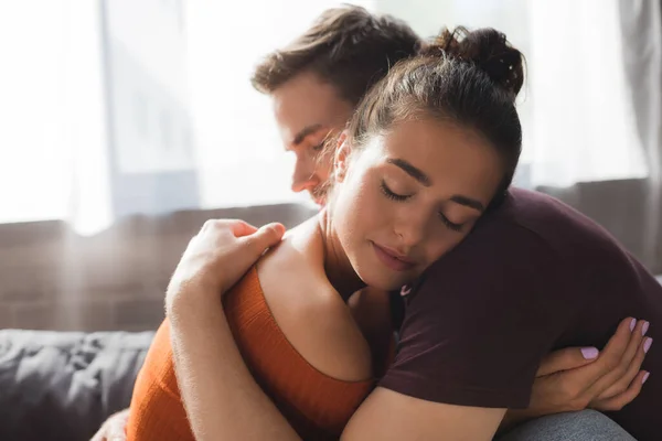 Jeune, tendre couple étreignant les yeux fermés tout en étant assis à la maison — Photo de stock