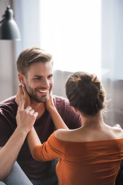 Vista posterior de la mujer joven abrazando el cuello de novio feliz mientras está de pie cara a cara en casa - foto de stock