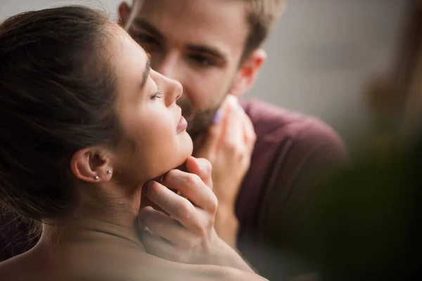 Tierno hombre tocando cara ow amada novia con los ojos cerrados sobre fondo borroso - foto de stock