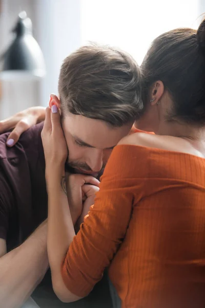 Back view of woman calming sad man holding hands near face with closed eyes — Stock Photo