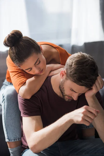 Young woman leaning on back of depressed boyfriend sitting with bowed head — Stock Photo