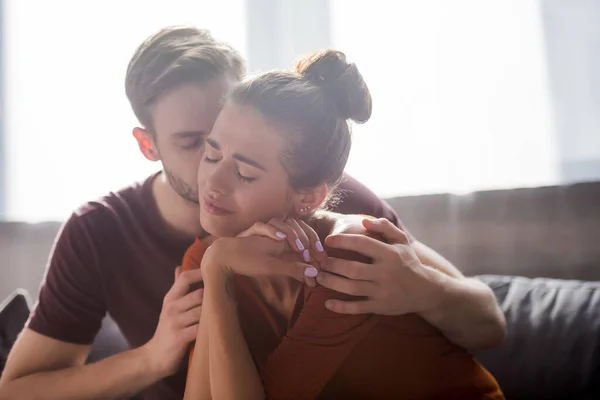 Responsive man hugging and calming worried girlfriend sitting with closed eyes — Stock Photo