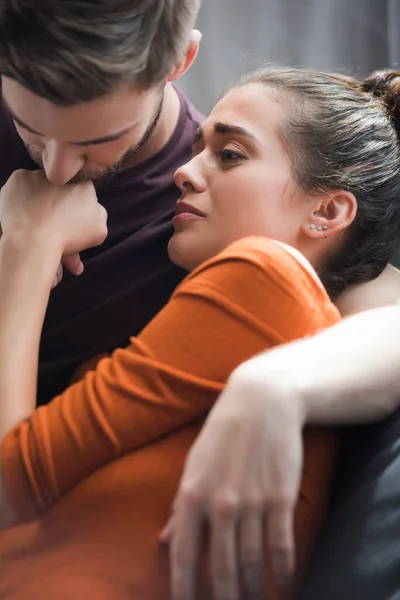 Responsive man kissing hand of upset girlfriend while calming her at home — Stock Photo