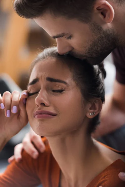 Homem responsivo beijando cabeça de choro namorada esfregando lágrimas com a mão — Fotografia de Stock