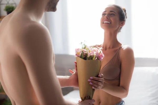 Happy woman taking flowers from shirtless man on blurred foreground — Stock Photo