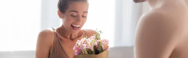 Excited woman holding bouquet near shirtless man on blurred foreground, banner — Stock Photo