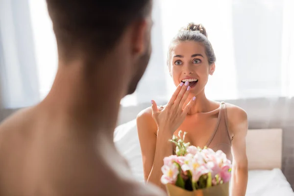 Surprised woman in bra covering mouth with hand while looking at man on blurred foreground — Stock Photo