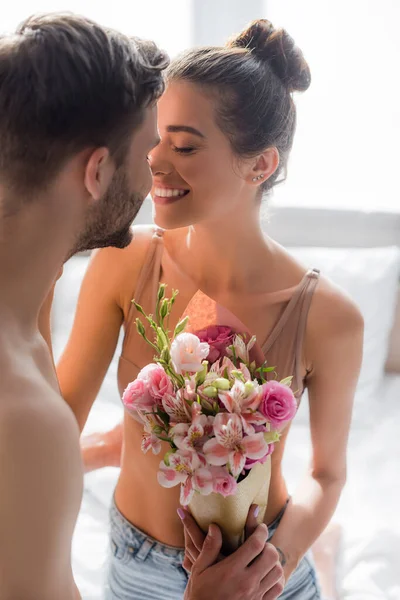 Sexy, happy woman standing face to face with man holding flowers in bedroom — Stock Photo
