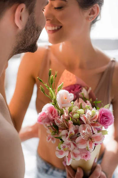 Hombre sosteniendo flores cerca sonriendo sexy novia sobre fondo borroso - foto de stock