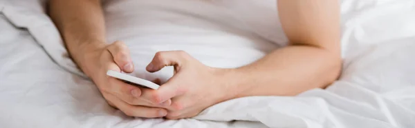 Обрезанный вид человека обмена сообщениями на мобильный телефон в постели, баннер — стоковое фото
