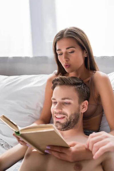 Sexy joven pareja leyendo libro en la cama juntos - foto de stock
