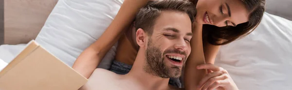 Hombre riendo tocando sensual novia sosteniendo libro en el dormitorio, bandera - foto de stock