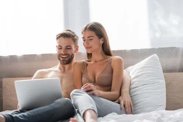 Молода пара посміхається, використовуючи ноутбук у спальні разом — стокове фото