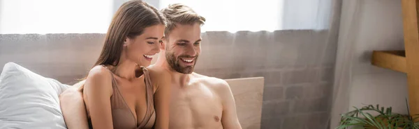 Весела сексуальна пара сміється, сидячи в спальні, банер — стокове фото