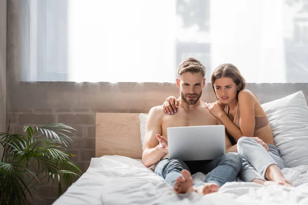 Schockierte Frau berührt hemdlosen Freund mit Laptop im Bett — Stockfoto