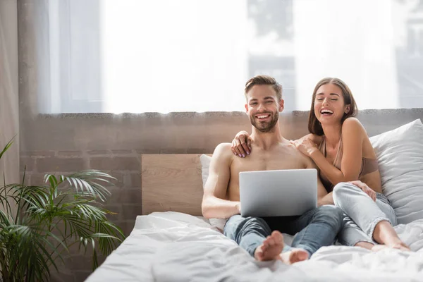 Riendo hombre y mujer usando el ordenador portátil juntos en el dormitorio - foto de stock