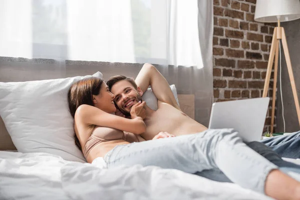 Mujer seductora en sujetador tocando la cara del novio sin camisa mientras yacen en la cama juntos - foto de stock