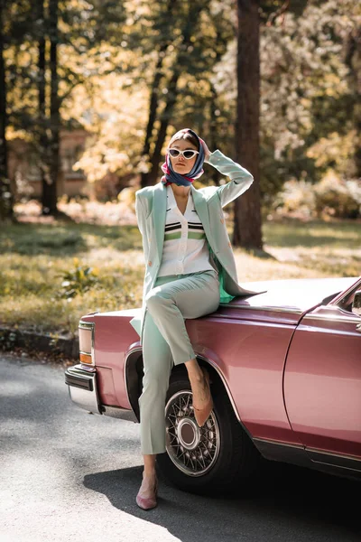 Елегантна жінка в сонцезахисних окулярах стоїть біля старовинного автомобіля на дорозі — стокове фото