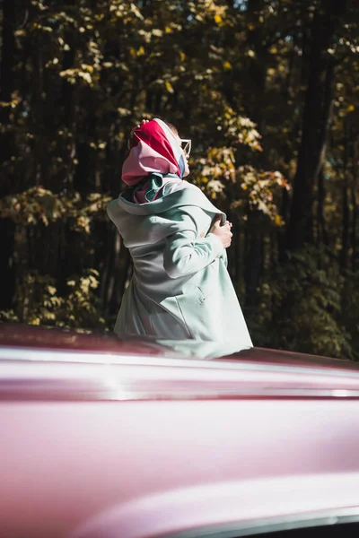 Visão traseira da mulher elegante em óculos de sol tocando jaqueta perto do carro ao ar livre — Fotografia de Stock