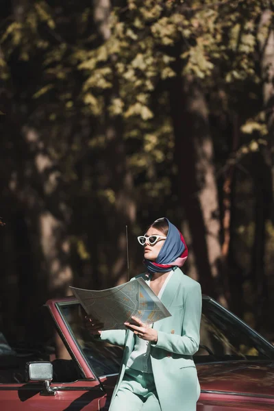 Junge stylische Frau hält Karte in der Hand und schaut in der Nähe von Retro-Auto im Freien weg — Stockfoto