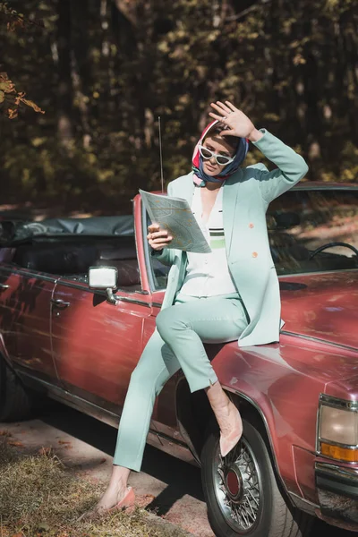 Stylish woman suffering from sunlight while holding map near car outdoors — Stock Photo