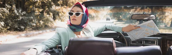 Femme élégante avec carte regardant loin en voiture sans toit pendant le voyage sur la route, bannière — Photo de stock
