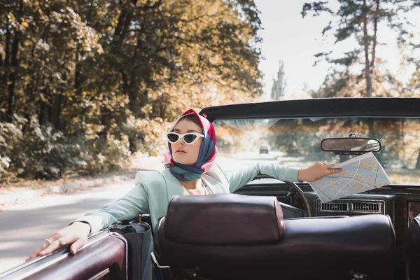 Elegante Frau mit Landkarte auf dem Fahrersitz eines dachlosen Autos im unscharfen Vordergrund — Stockfoto