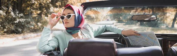 Frau mit Landkarte berührt Sonnenbrille in dachlosem Auto auf verschwommenem Vordergrund, Banner — Stockfoto