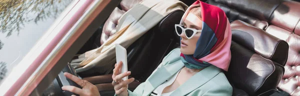 Femme à la mode utilisant un smartphone tout en conduisant une voiture cabriolet au premier plan flou, bannière — Photo de stock