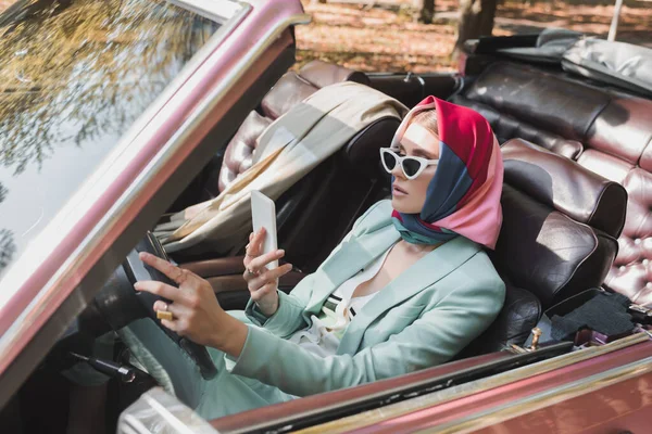 Mulher elegante usando smartphone enquanto dirige carro sem telhado em primeiro plano desfocado — Fotografia de Stock