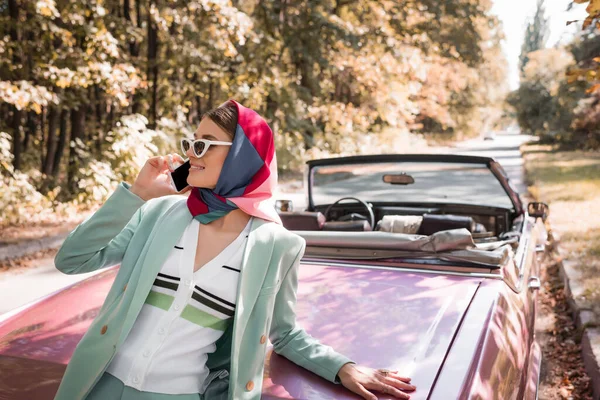 Femme élégante souriant tout en parlant sur smartphone près de toit auto sur la route — Photo de stock