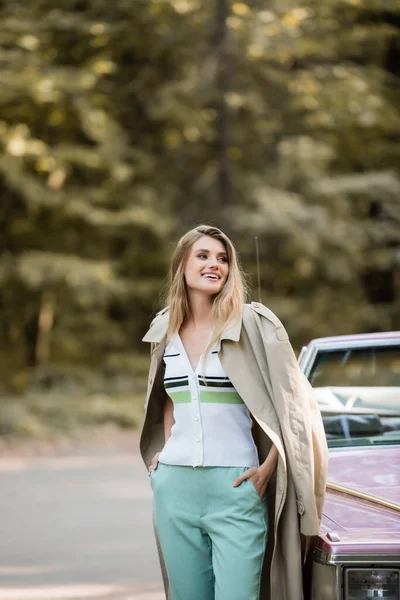 Lächelnde Frau, die wegschaut, während sie mit Händen in Taschen in der Nähe des Cabrios steht — Stockfoto