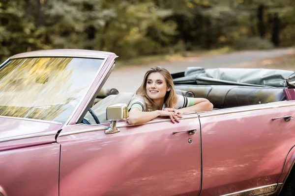 Joyeuse jeune femme regardant loin tout en étant assis dans la voiture convertible — Photo de stock