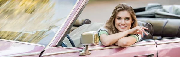 Alegre joven mujer sonriendo a la cámara mientras está sentado en un coche descapotable, pancarta - foto de stock