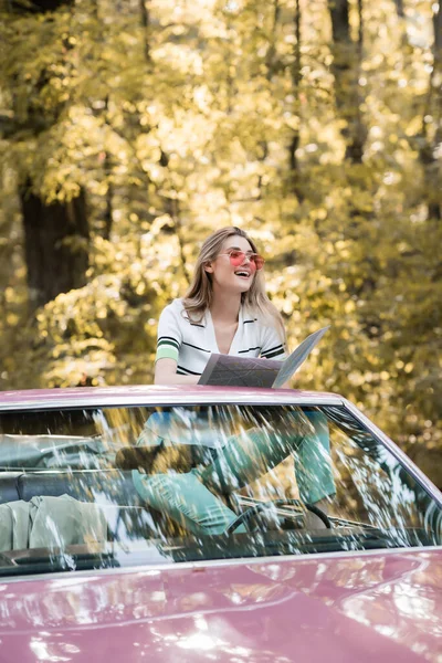 Mulher alegre olhando embora enquanto segurando mapa em cabriolet — Fotografia de Stock