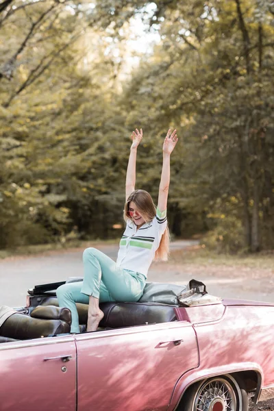 Aufgeregte barfüßige Frau sitzt im Cabrio, die Hände in der Luft — Stockfoto