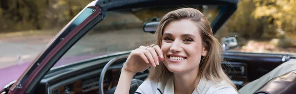 Cheerful woman looking at camera while sitting in cabriolet, banner — Stock Photo