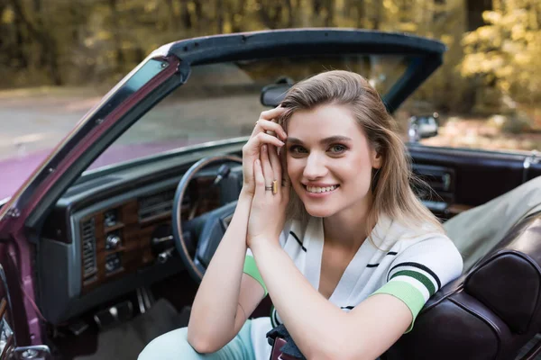 Femme gaie tenant la main près du visage tout en regardant la caméra de cabriolet vintage — Photo de stock