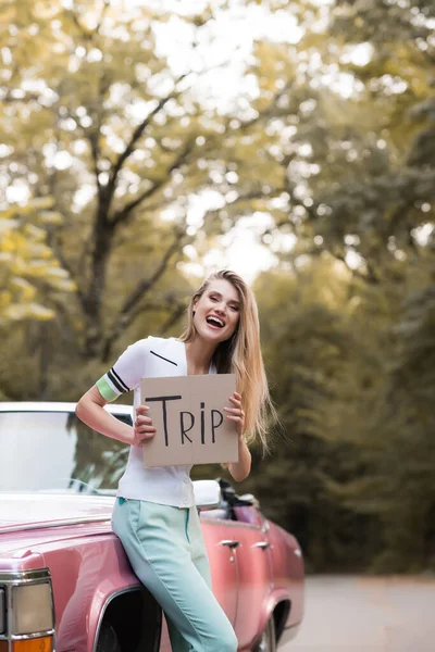 Animado mulher segurando cartão com viagem lettering perto de cabriolet vintage — Fotografia de Stock