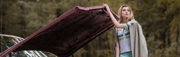 Giovane donna che distoglie lo sguardo mentre apre il cofano di un'auto d'epoca rotta, banner — Foto stock