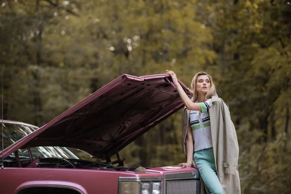 Jovem mulher olhando embora enquanto a abertura capuz de carro retro quebrado — Fotografia de Stock